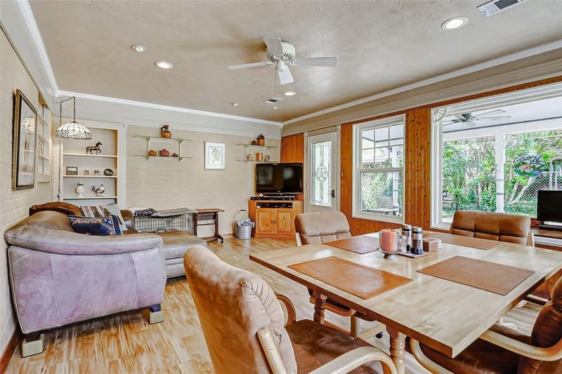 Bright room with wood-look floors, ceiling fan, built-in shelves, dining table and large windows onto a covered patio
