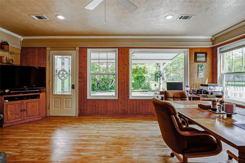 Wood-paneled room with a glass door with a star design, large windows onto a covered patio, and wood-look floor