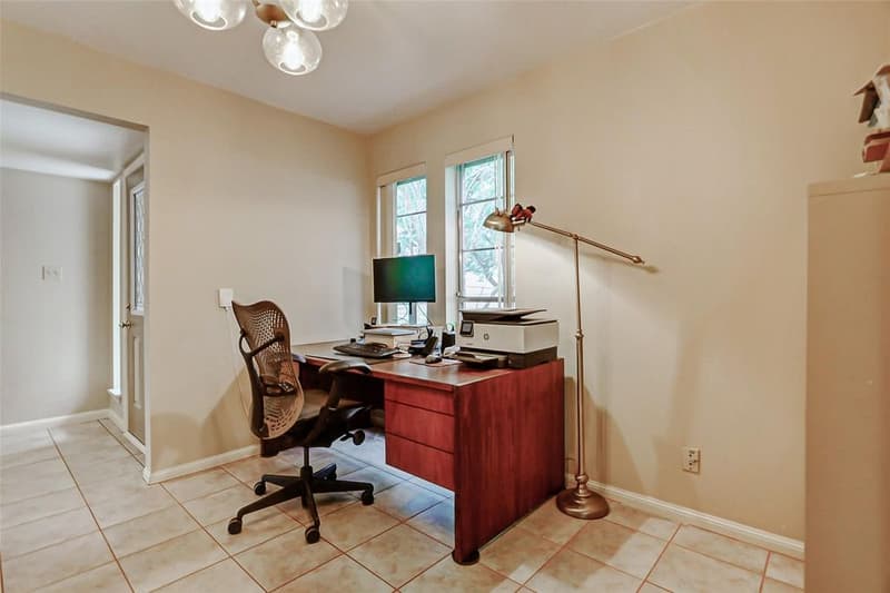 Room with tile floor and two windows, set up as a home office with a desk, mesh chair and floor lamp