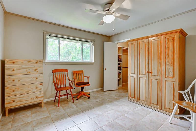 Bedroom with tile floor, ceiling fan, window facing green trees, and open door to a shelved walk-in closet