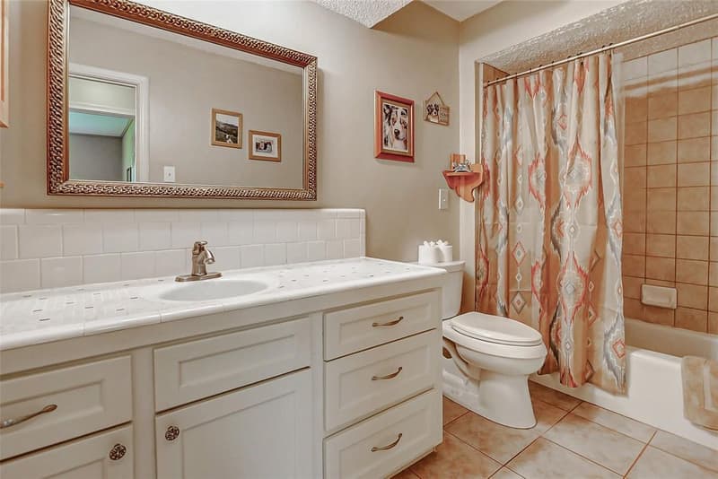 Bathroom with white vanity, framed mirror, tile backsplash, toilet, and tiled tub/shower combo with curtain