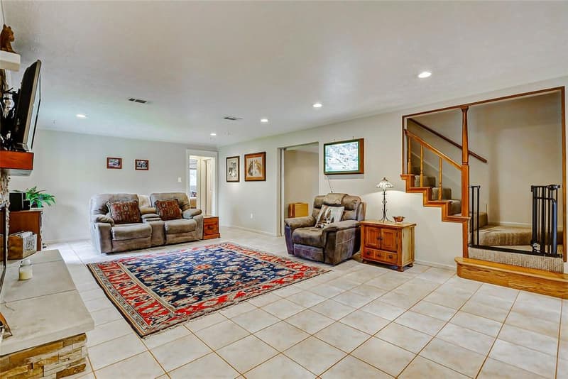 Large living room with tile floor, recessed lights, stone fireplace hearth, recliners, area rug, and staircase to second floor