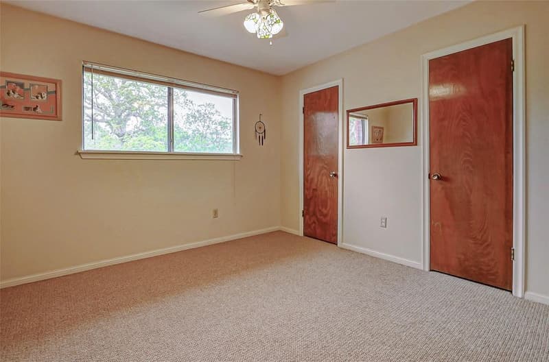 Carpeted bedroom with ceiling fan, window framing mature trees, wall mirror, and two wood-grain doors