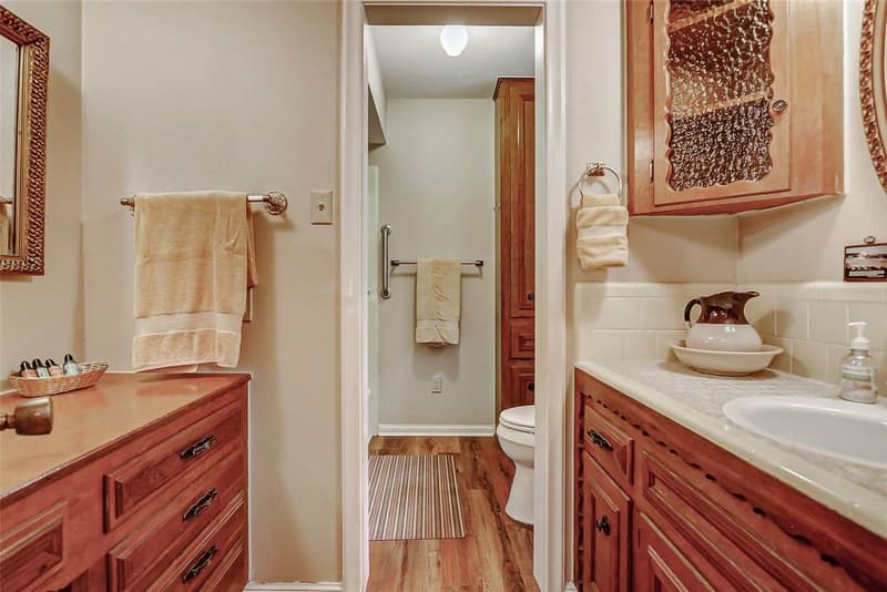 Bathroom vanity area with two wood cabinets, framed mirrors, and doorway to a separate toilet room with wood-look floor