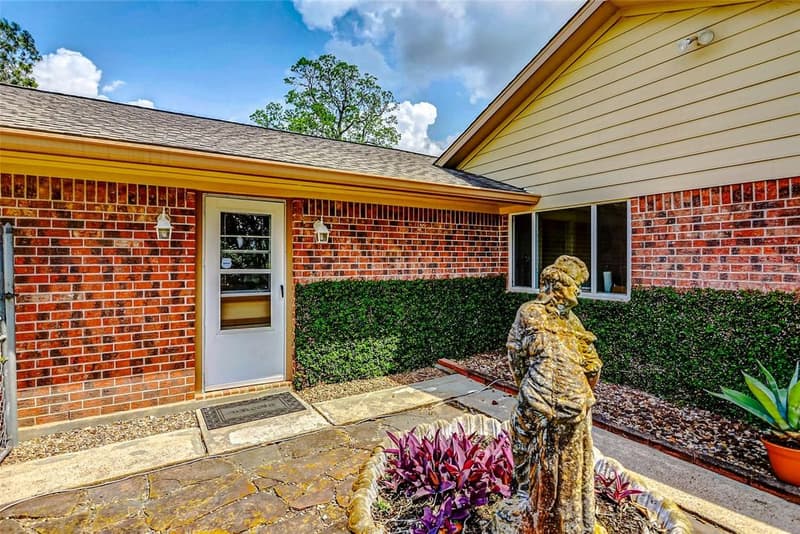 Brick entry with white glass storm door, flagstone walkway, hedge, and a statue fountain planted with purple flowers