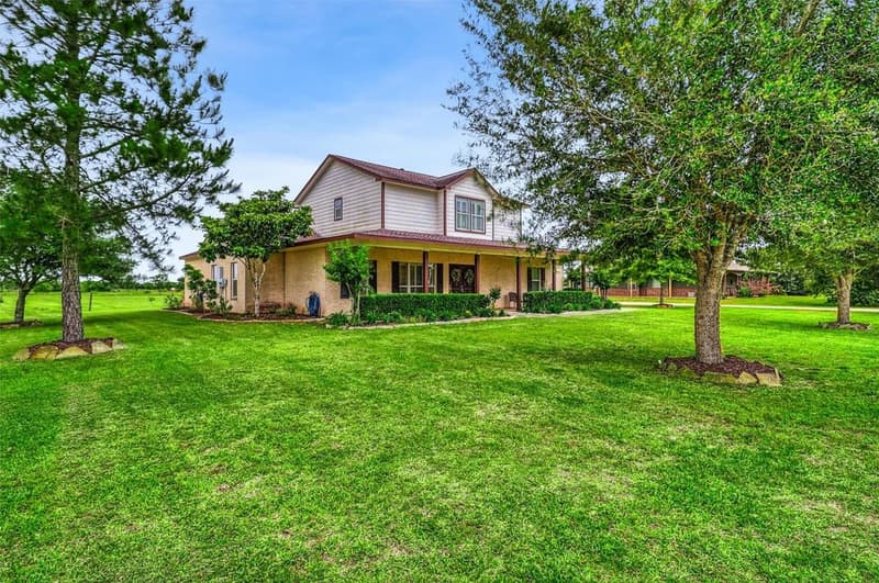 Two-story brick and siding home with a covered front porch, set back on a wide green lawn with mature trees