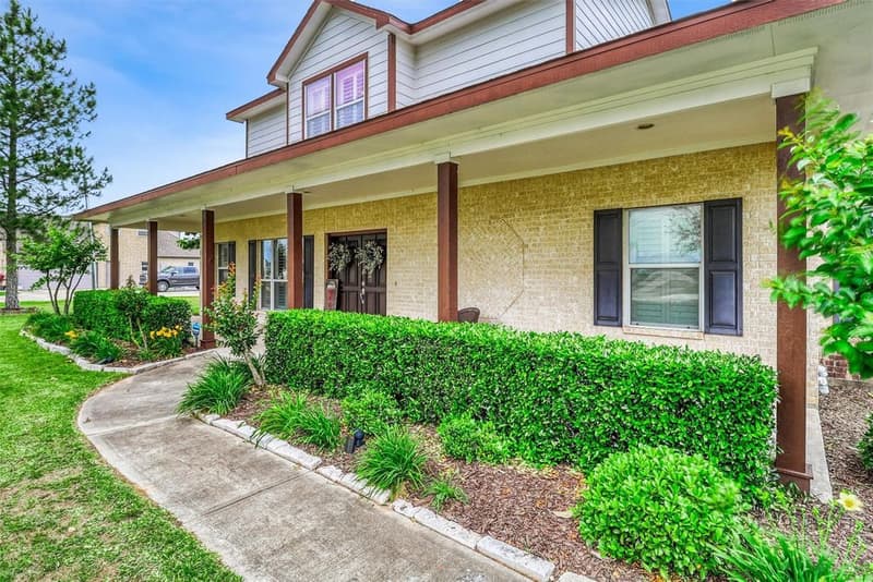 Covered front porch with wood posts, double front doors, dark shutters and a curved walkway lined with shrubs