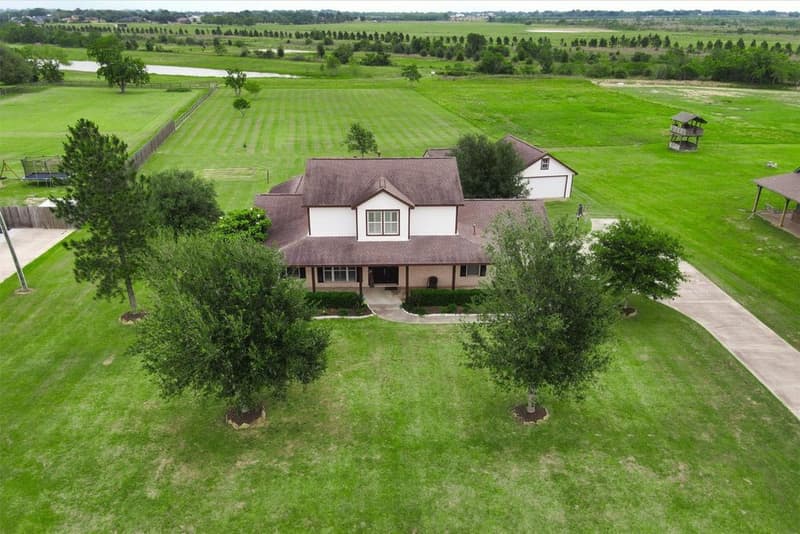 Aerial view of the two-story home on an open acreage lot, a detached building behind it and a pond and fields beyond