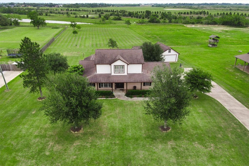 Aerial view of the two-story home on an open acreage lot, a detached building behind it and a pond and fields beyond