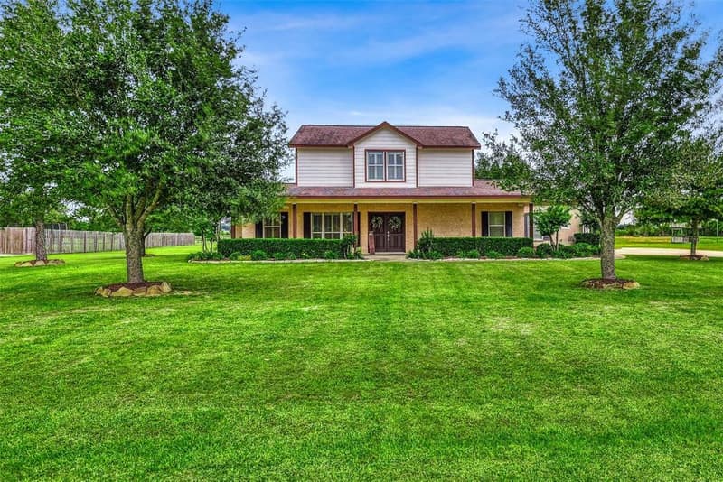 Front view of a two-story brick home with shuttered windows, double front doors and a large mowed lawn with trees