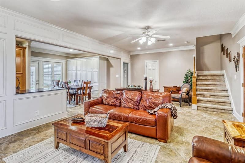 Living area with tile floor and ceiling fan, open to a dining area with a wall of white built-in cabinets