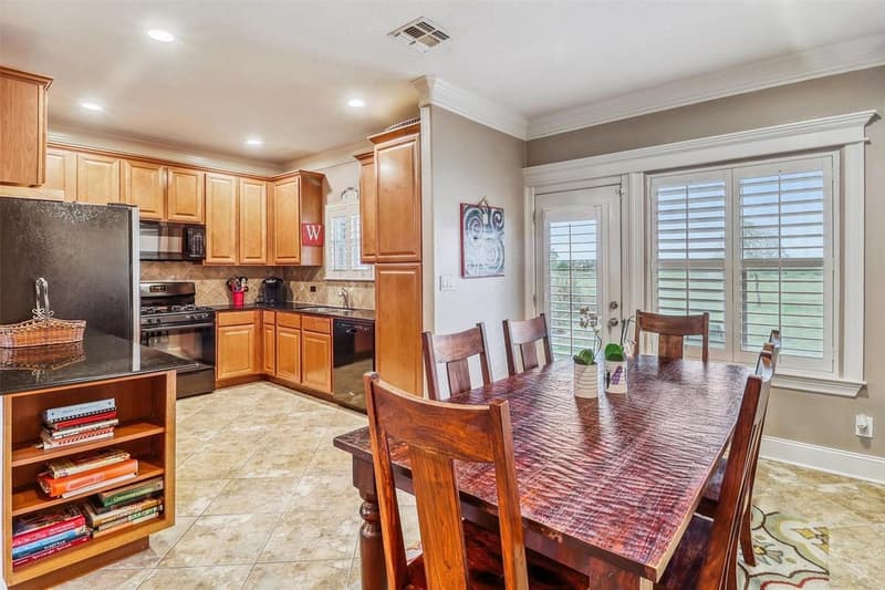 Kitchen with wood cabinets, dark counters and tile backsplash beside a dining area with shuttered windows and a door