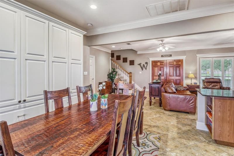 Dining area with a wall of white built-in cabinets, tile floor and a view into the living room and staircase