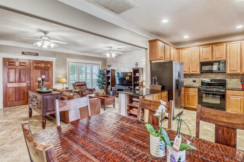 Open kitchen with wood cabinets, stainless refrigerator and black gas range, looking into the living room