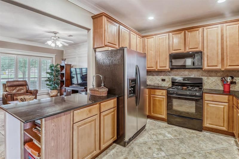 Kitchen peninsula with dark granite and open bookshelf end, wood cabinetry, gas range and diagonal tile backsplash