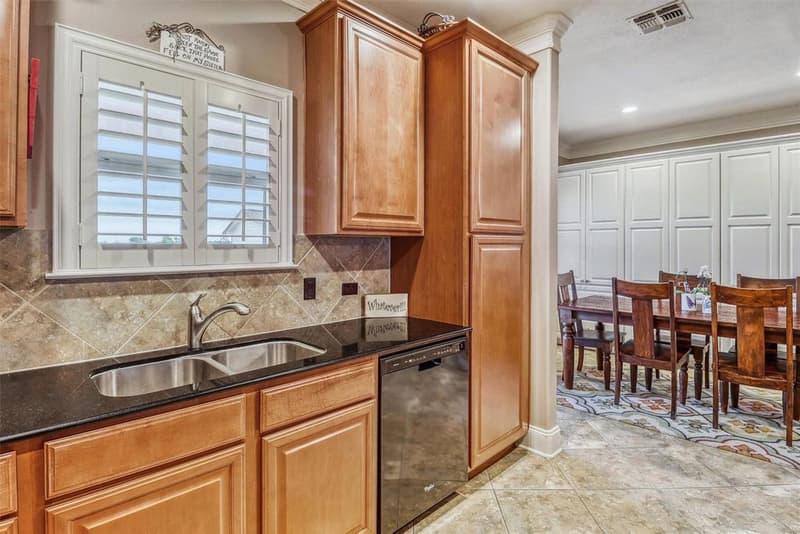 Kitchen sink with shuttered window and tall wood cabinets, next to the dining area with white built-in cabinets