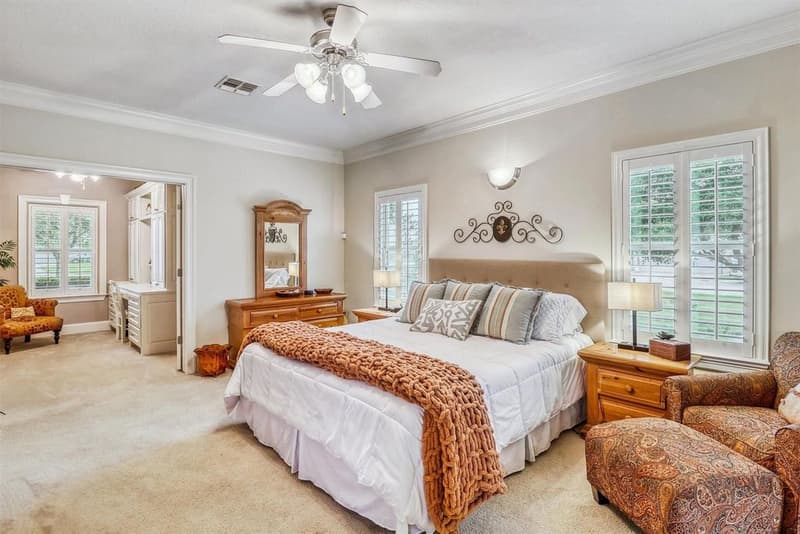Primary bedroom with plantation shutters, ceiling fan and an open doorway to an adjoining room with built-in desk cabinetry