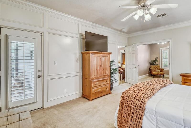 Primary bedroom wall with raised decorative wall panels, an exterior door with shutters, and double doors to the hall