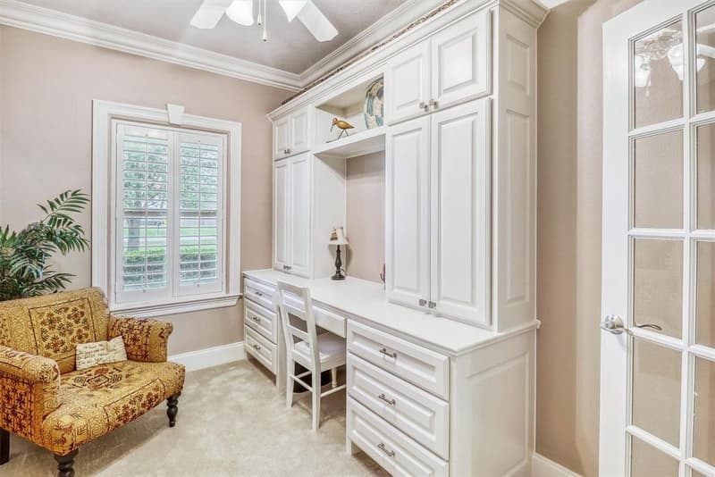 Small office with white built-in desk, upper cabinets and drawers, a shuttered window and a glass-paned French door