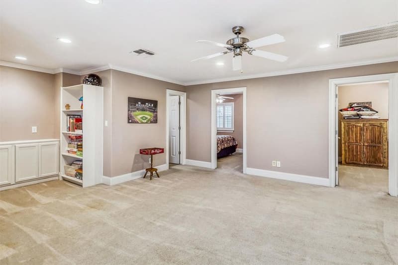 Carpeted upstairs game room with built-in low cabinets, a bookshelf, ceiling fan and doors to adjoining rooms