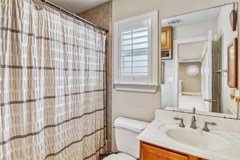 Upstairs bathroom with tub/shower behind a curtain, single-sink vanity and a shuttered window