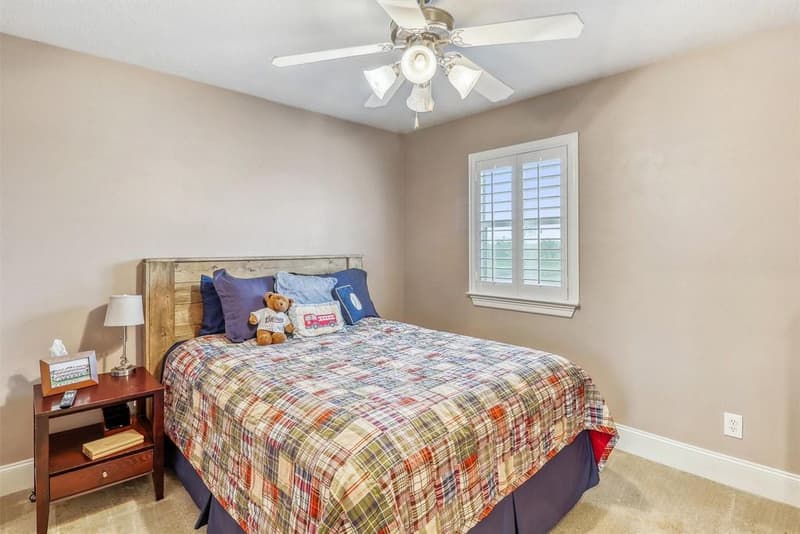 Upstairs bedroom with a queen bed, ceiling fan, carpet and a window with plantation shutters