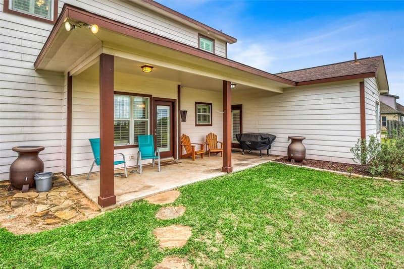 Covered back patio with chairs and a grill, a lawn and stepping stones in front