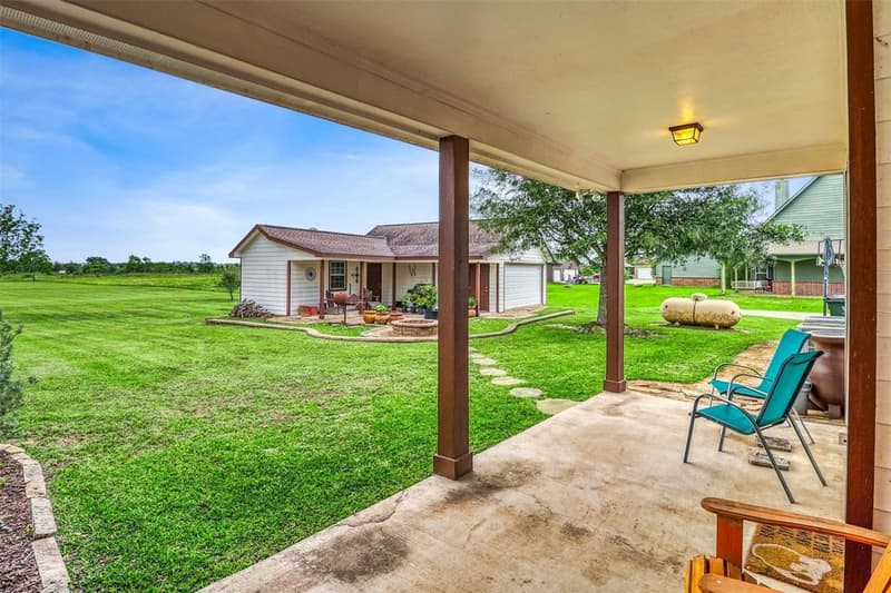 View from covered back patio across the lawn to the detached building, a fire pit and a propane tank