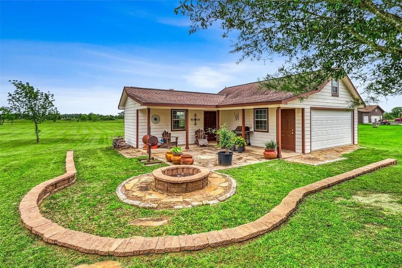 Detached building with covered porch, two entry doors, garage door and flagstone patio, a round block fire pit on the lawn in front