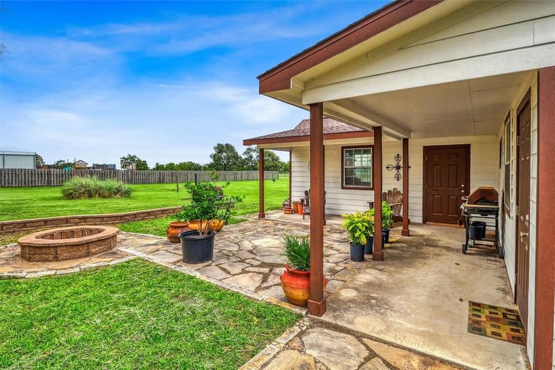 Covered porch of the detached building with a flagstone patio, fire pit, potted plants and a wide green lawn beyond
