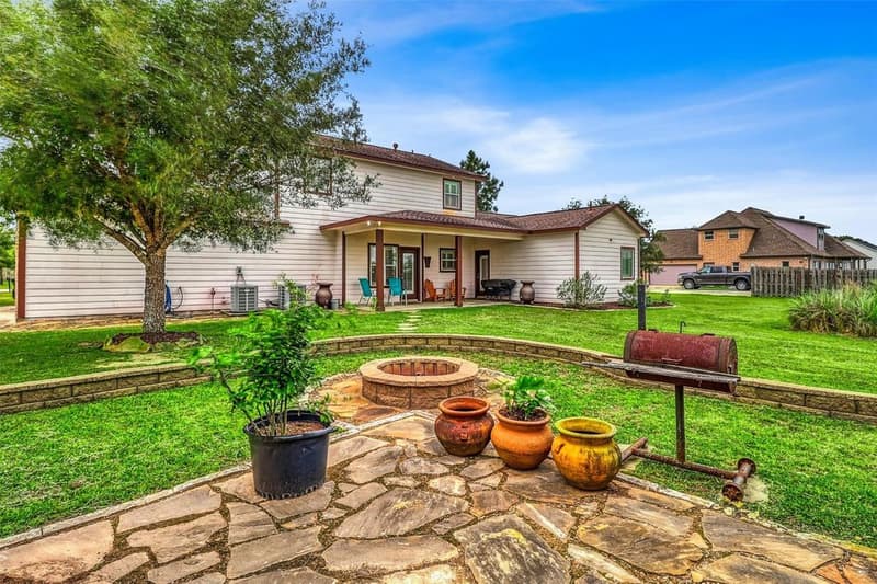 Rear of the two-story home with covered back patio, seen across a flagstone patio with a round block fire pit and curved retaining wall