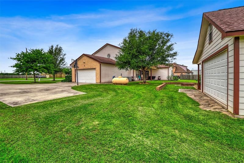 Side yard lawn between the main home's attached garage and the detached building's garage door, with the concrete driveway at left