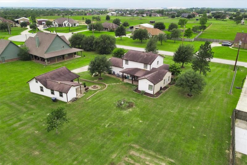 Drone view of the two-story home and detached building on a large open lot, with neighboring acreage homes and fields beyond