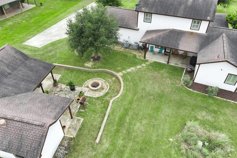 Overhead drone view of the backyard showing the covered back patio, stepping-stone path, curved retaining wall, fire pit and flagstone patio