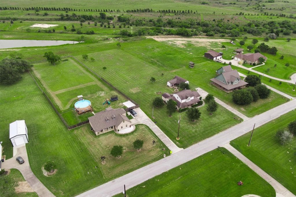 Aerial view of homes on acreage lots in Settlers Estates near Sealy, with open pasture, tree lines and a pond