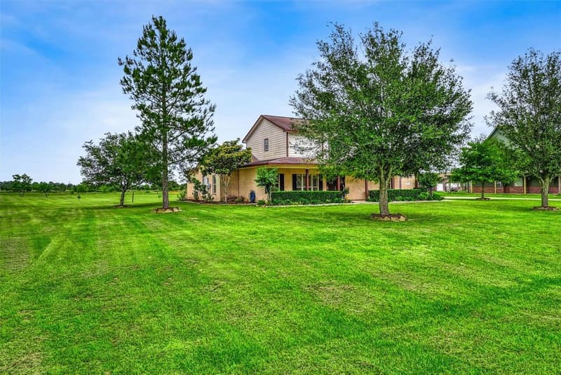 Side view of the home framed by mature trees and a pine, with a wide freshly mowed lawn stretching toward open land